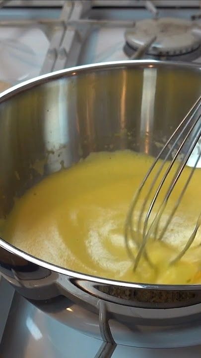 Visp rører en gul saus i en blank kasserolle på komfyren